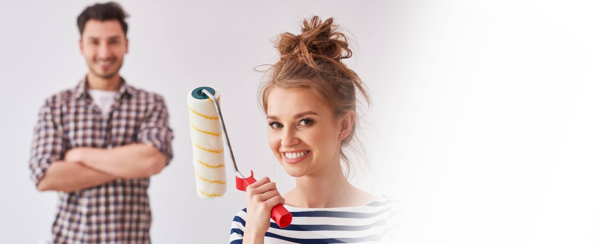 Kobieta trzymająca wałek do malowania, w oddali mężczyzna